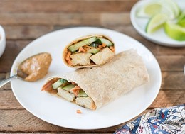 wrap stuffed with vegetables next to a spoon with peanut butter.