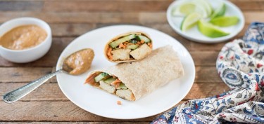 wrap stuffed with vegetables next to a spoon with peanut butter.