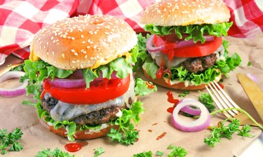 a tall burger with meat, sauce, tomatoes, red onions, lettuce and dripping cheese.