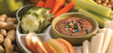 a tray of fruits and vegetables with a chocolate dip in the middle.