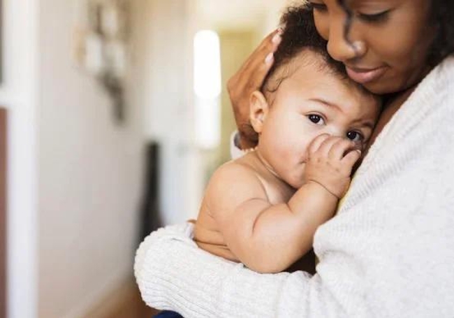 a mother cradling softly her babies head against her chest