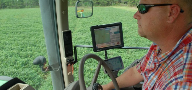 A farmer in a tractor inspecting the crops with help of a GPS device.