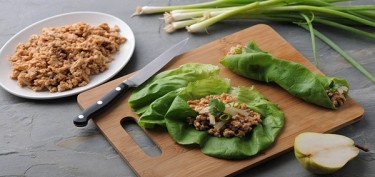 open lettuce leaves filled with meat on top of a board.