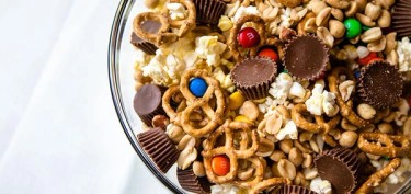 a bowl of popcorn topped with pretzels, peanuts and chocolate candies.