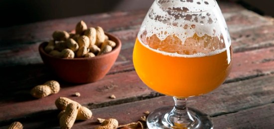 a glass of beer besides a bowl of peanuts.