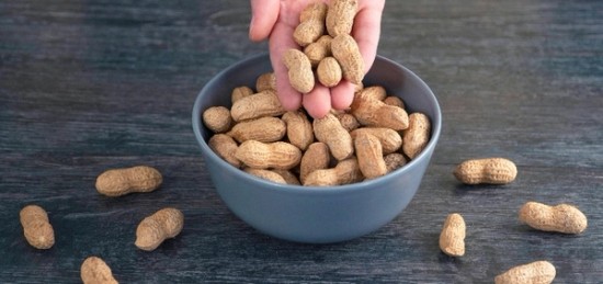 a person reaching for unshelled peanuts in a blue bowl.