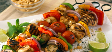 roasted chicken and vegetables skewers on top of white rice.