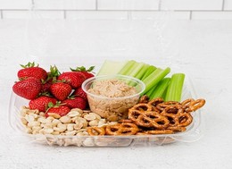 a tray filled with peanuts, pretzels, strawberries and celery with a dip sauce in the middle.