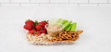a tray filled with peanuts, pretzels, strawberries and celery with a dip sauce in the middle.