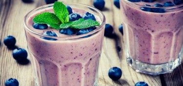 two glasses of blueberry smoothie decorated with a mint on top.