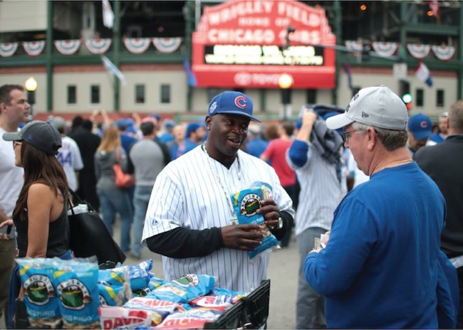 a man in a baseball cap holding a peanut package in front of a stadium