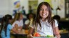 A young girl holding a plate of food in a school cafeteria.
