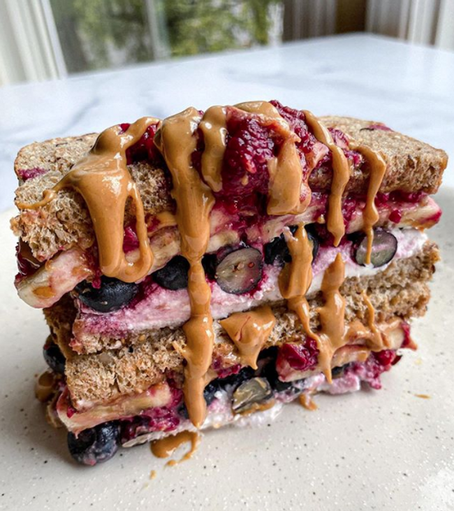 Stacked bread slices filled with jam, fruits and drizzled in peanut butter.