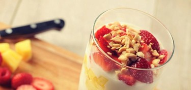 a glass filled with yogurt, chopped fruits and peanuts on top.