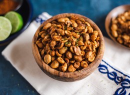 Bowl of chili lime peanuts on white and blue embroidered napkin, limes and chili powder in background