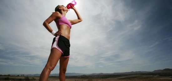 a woman dressed in workout clothing drinking water.