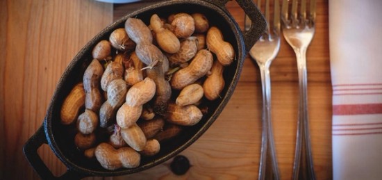 Unshelled peanuts in a cast iron pan over a wooden table.