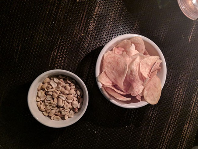 a restaurant table holding a bowl of peanuts next to one of chips