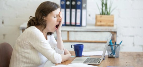 a woman yawning with a laptop in front of her.