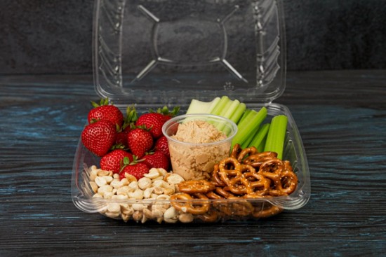 school lunch on a wood table with strawberries, celery, pretzels, peanuts and peanut butter hummus