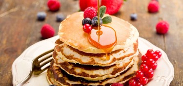 a stack of pancakes with raspberries on top drizzled with honey.