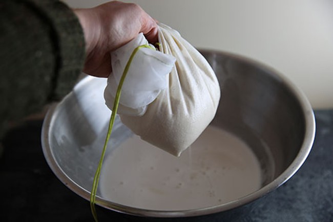 a person holding a nut milk bag over a big bowl
