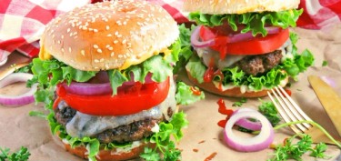 a tall burger with meat, sauce, tomatoes, red onions, lettuce and dripping cheese.