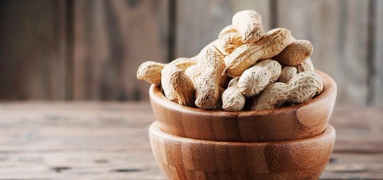 a wooden bowl filled with unshelled peanuts on top.