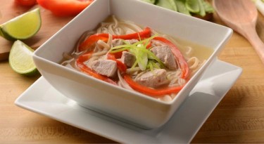 bowl of noodle soup with chicken and red pepper.