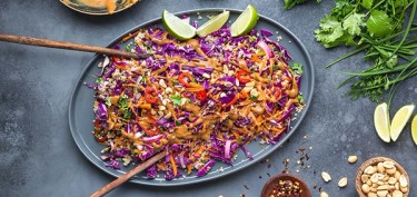 a large platter full of shredded red cabbage and carrots drizzled in a peanut butter sauce.