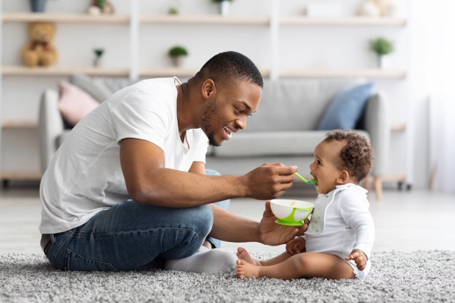 Loving Black Dad Feeding His Cute Baby Son At Home