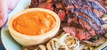 slices of medium steak and roasted onions next to a dip sauce.