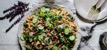 a plate of pasta with cucumbers, nuts and herbs.