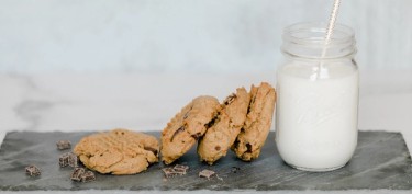 a glass of milk next to four chocolate chips cookies.