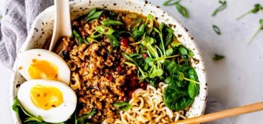 noodles topped with a lot of ground pork, green leaves and a boiled egg cut in half.