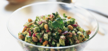 a glass bowl full of chopped cuccumbers, peanuts and red onions.