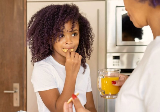 Young child enjoying a cookie with an adult woman holding a glass of orange juice and another cookie.