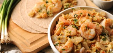 a bowl filled with shrimp and finely sliced peanuts next to tortilla wraps.
