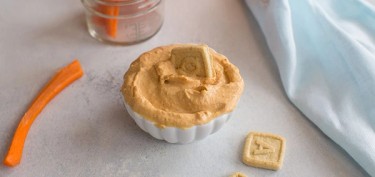 a small kids bowl filled with a peanut dip next to cutted carrots.