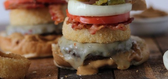 A burger topped with a thick slice of onion, tomato, and bacon.