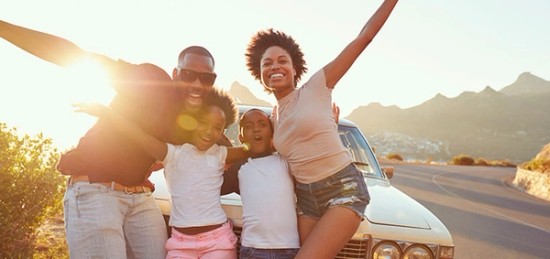 A man and woman and their two kids are posing for a picture in front of a car.