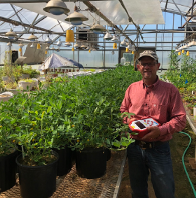 Man standing in a greenhouse surrounded by plants.