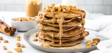 a stack of pancakes with peanut butter drizzled on top.