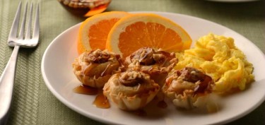 a plate topped with small tartlet shells filled with pancakes next to scrambled eggs and orange slices.