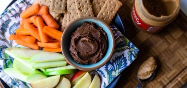 a plate of crackers, carrots, apples, celery, and chocolate hummus.