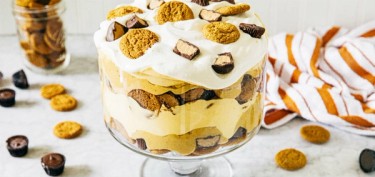 a glass cake jar filled with layers of cream, cookies and chocolate pieces.