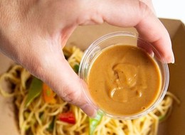 a person holding a container of sauce over a plate of pasta.