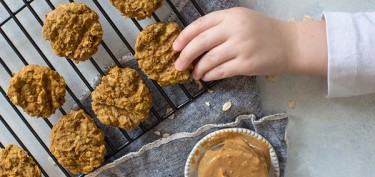 a kid reaching out to a cookie in a cooling tray.