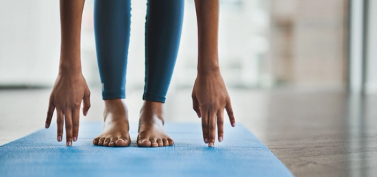 A bended woman touching her feet with her arms on a yoga mat.