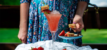 a strawberry and pastry on top of a tall glass with martini on ice.